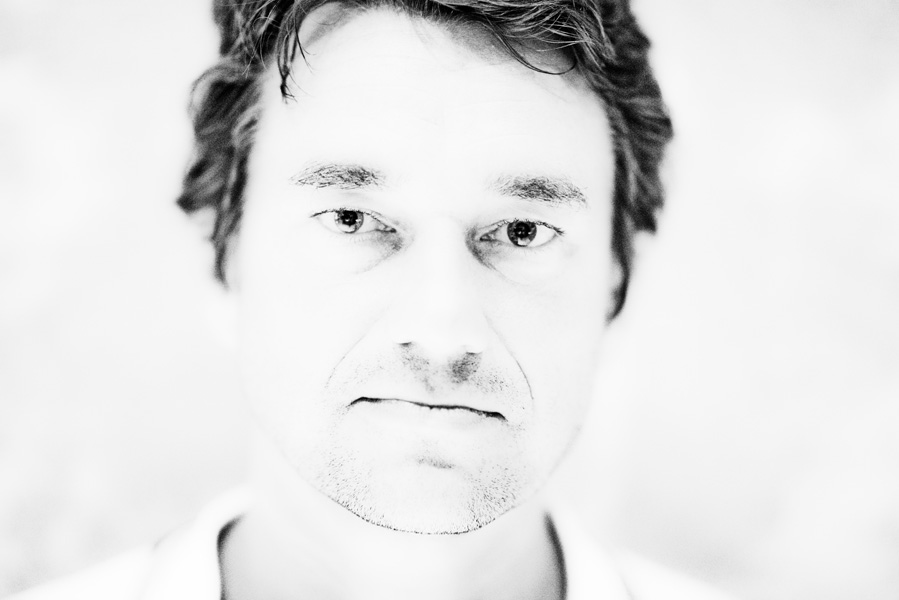 Mann mittleren Alters mit kurzem Haar blickt direkt in die Kamera, Nahaufnahme in Schwarz-Weiß mit hohem Kontrast.