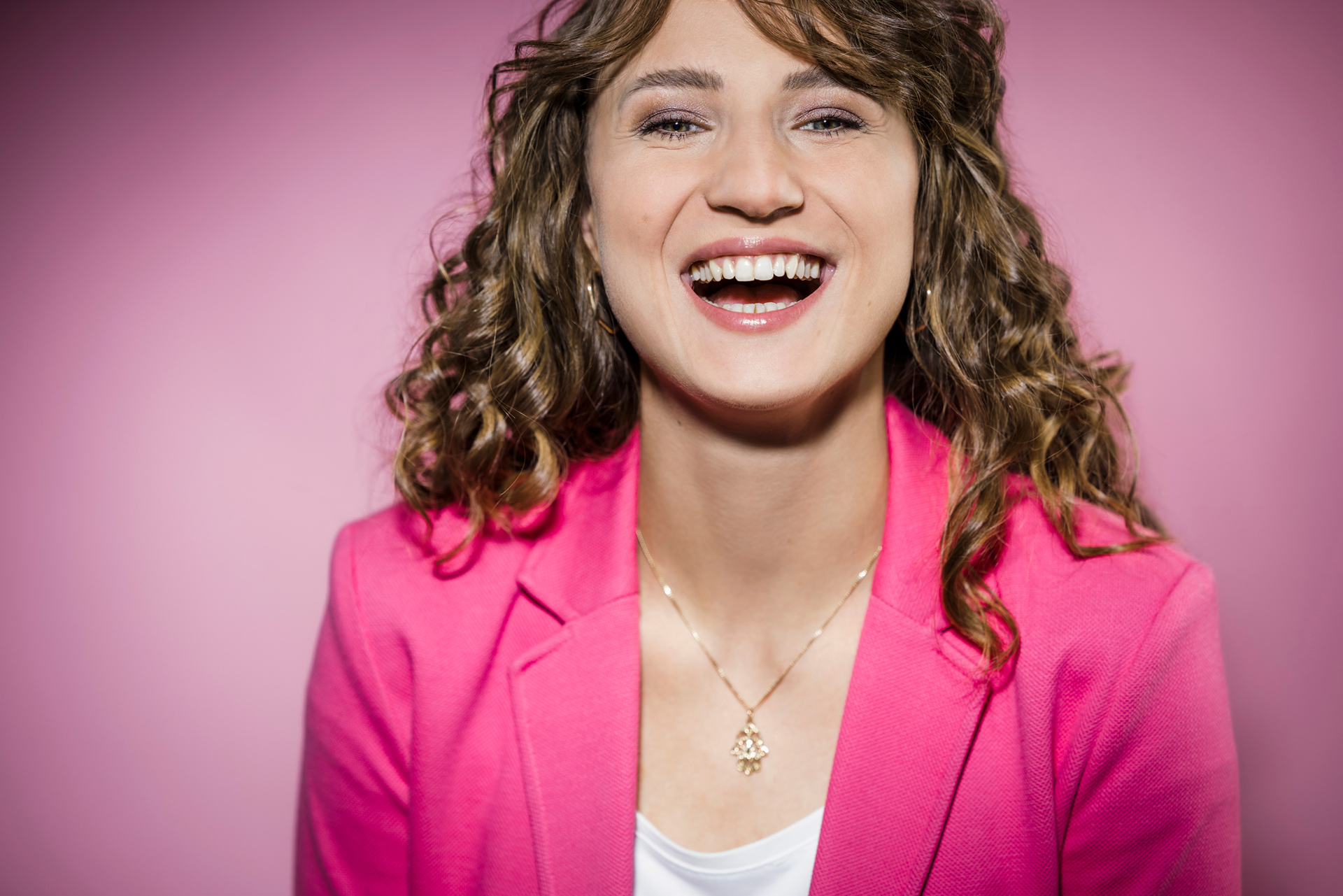 Portraitfotograf Jochen Rolfes aus Düsseldorf mit Portraitfotografie: Portrait im Studio mit pinken Blazer, vor pinken Hintergrund, Lachen