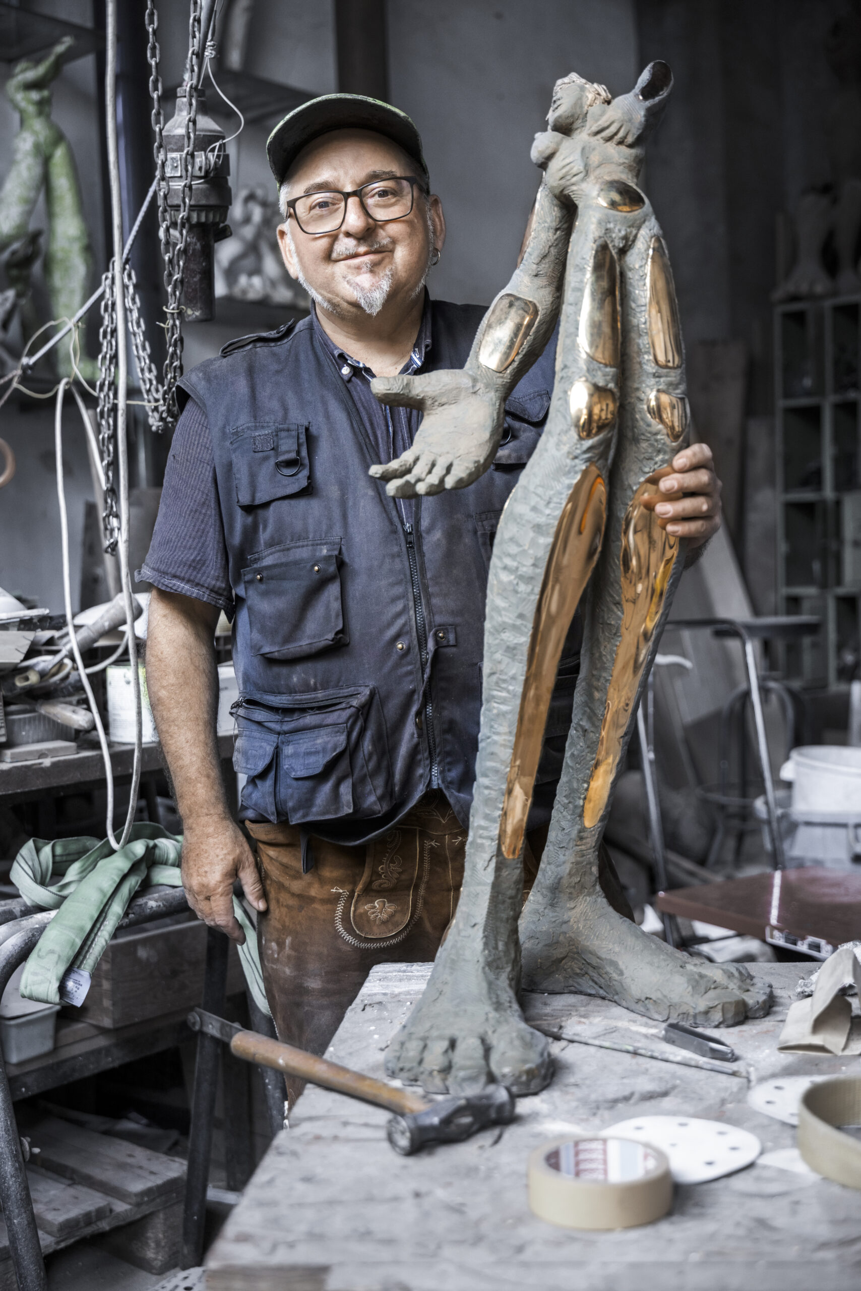 Künstler Jörg W. Schirmer steht hinter seinen Kunstwerken. Der Künstler hat eine Cap an und der Hintergrund ist dunkel.