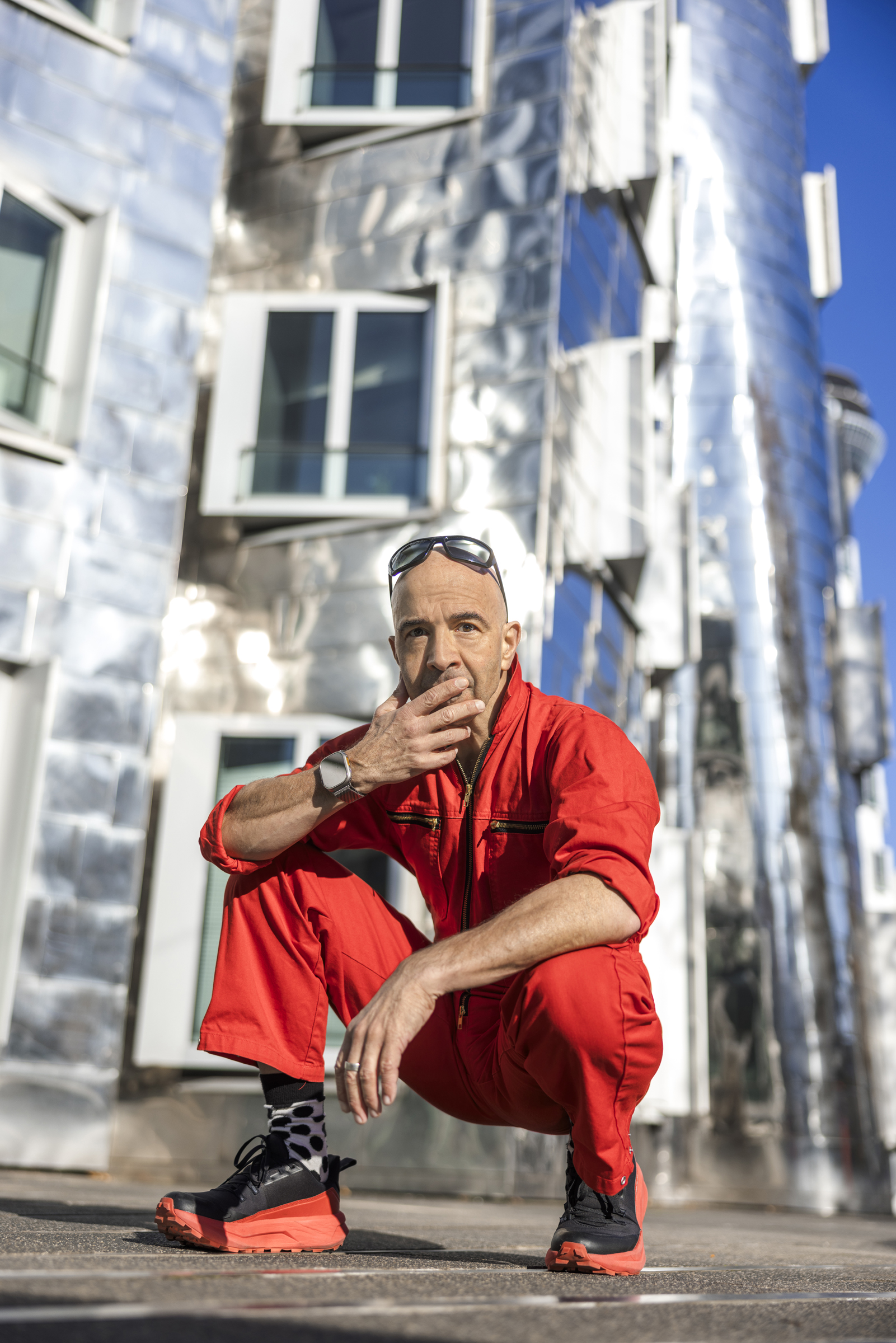 Künstler Michael Oliver Flüß hockt vor einem der Gerhy Bauten im roten Overall und Sonnenbrille.